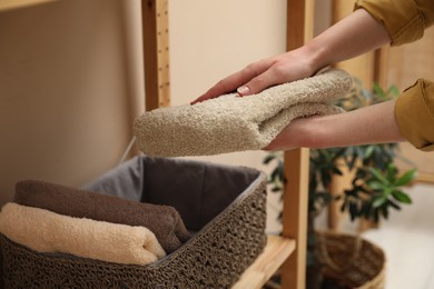 Photo of Woman putting towel into storage basket indoors, closeup