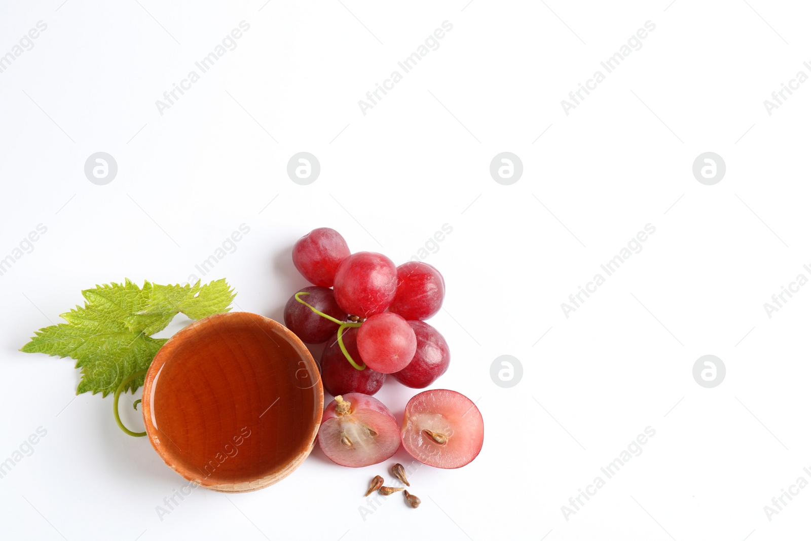 Photo of Organic red grapes, seeds and bowl of natural essential oil on white background, flat lay. Space for text