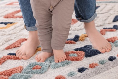 Mother supporting her baby son while he learning to walk on carpet, closeup