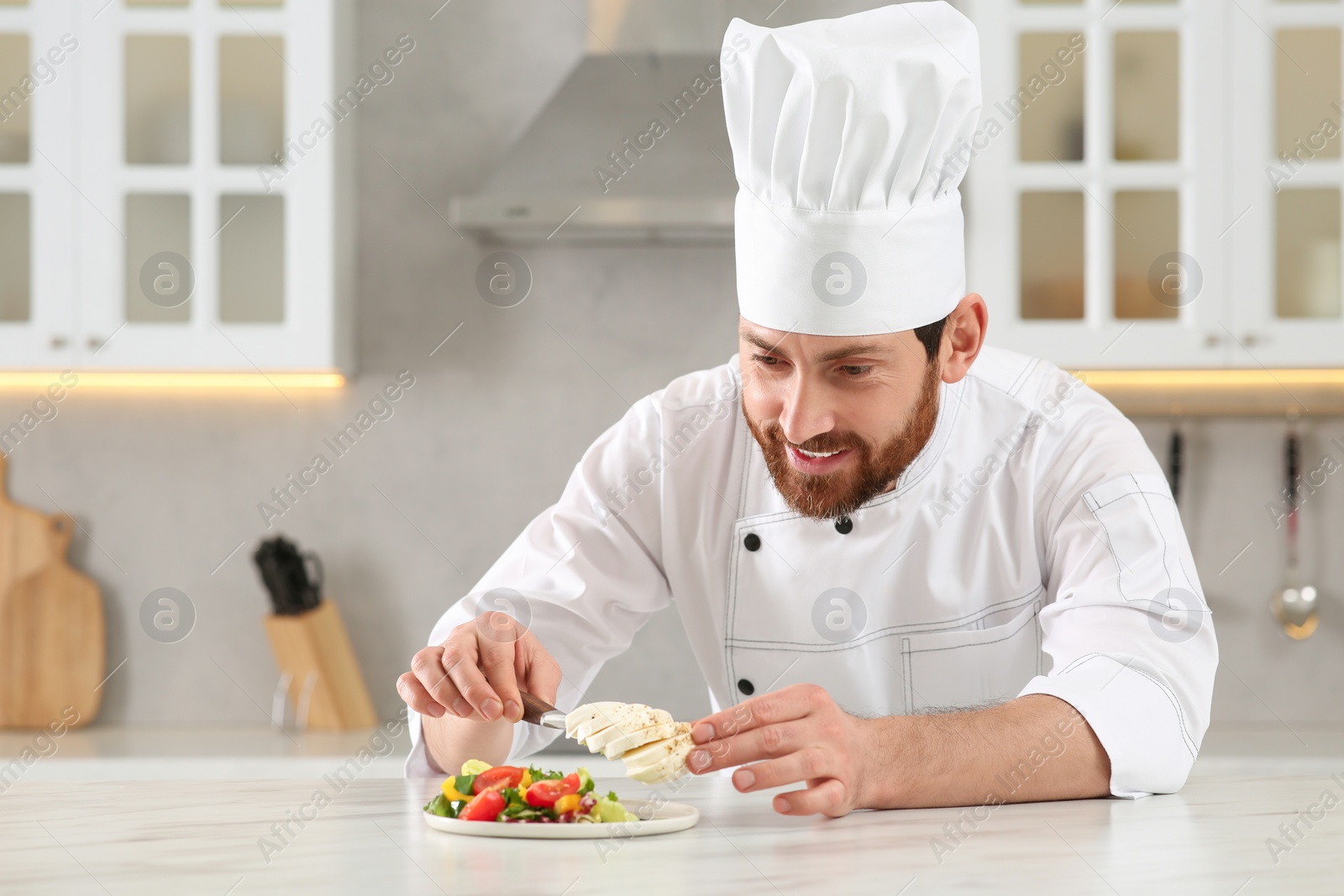 Photo of Professional chef adding mozzarella into delicious salad at marble table in kitchen