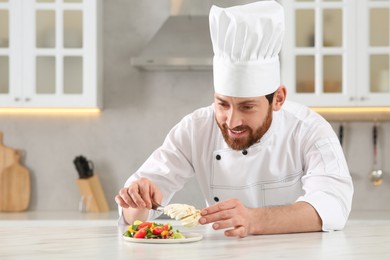 Professional chef adding mozzarella into delicious salad at marble table in kitchen