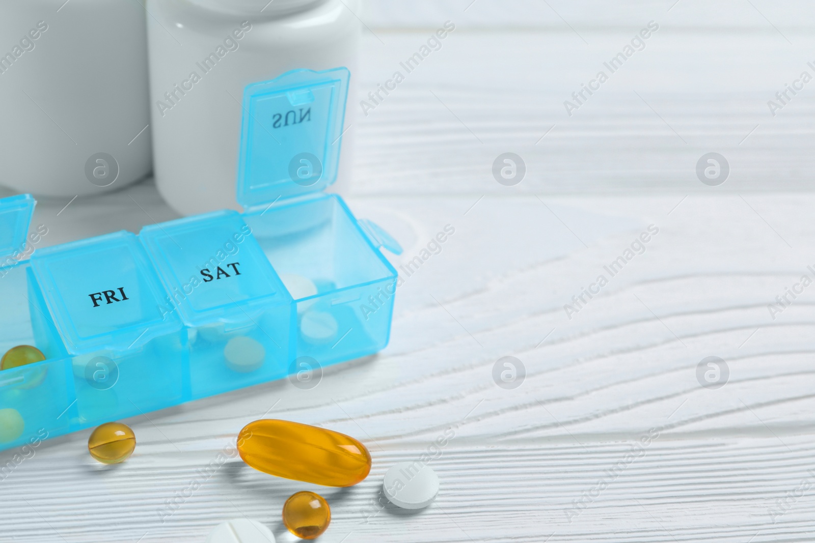 Photo of Weekly pill box with medicaments on white wooden table, closeup. Space for text