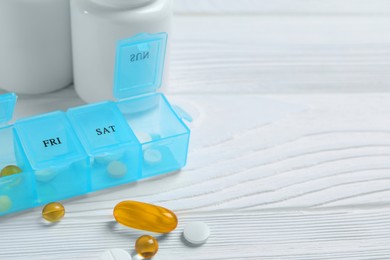 Photo of Weekly pill box with medicaments on white wooden table, closeup. Space for text