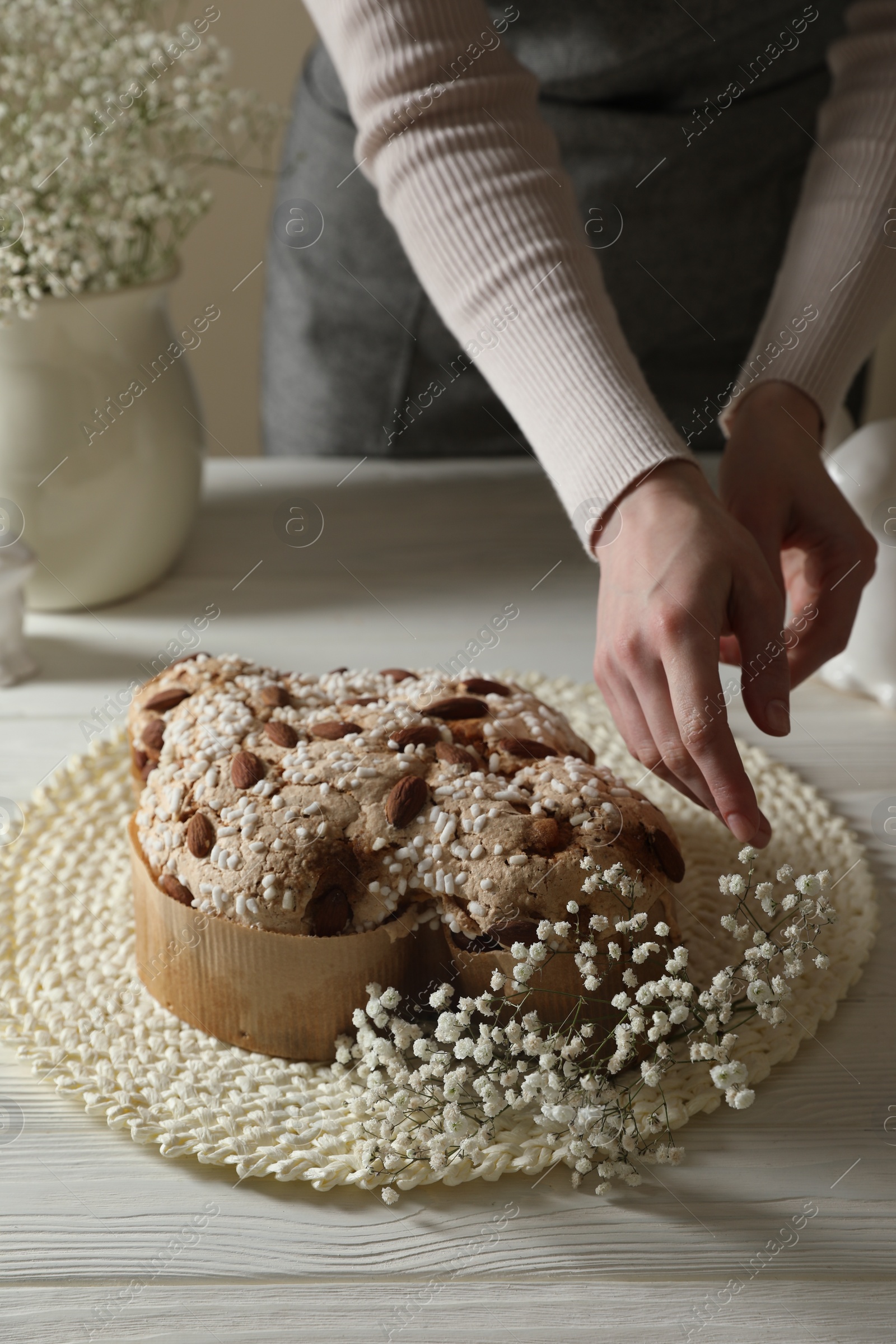 Photo of Woman decorating delicious Italian Easter dove cake (traditional Colomba di Pasqua) with flowers at white wooden table, closeup