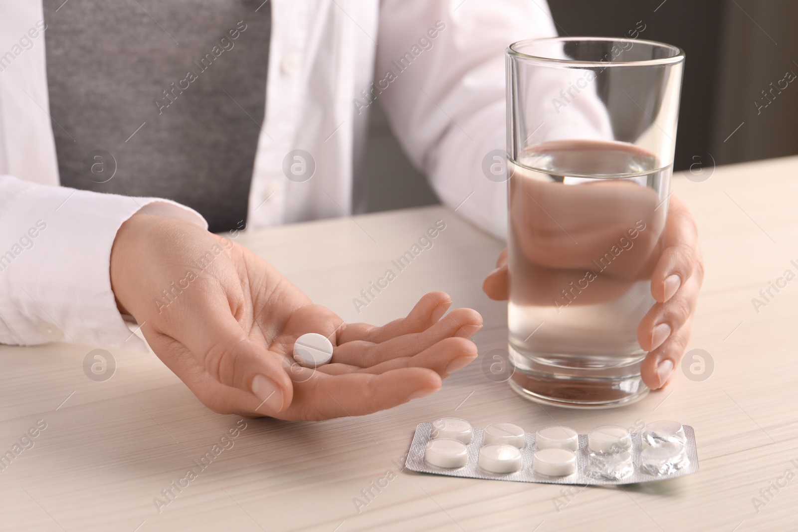 Photo of Woman with pills and glass of water at white wooden table, closeup