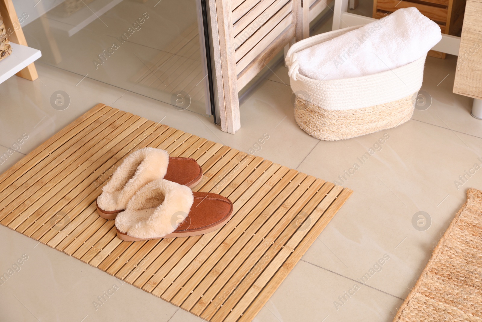 Photo of Wooden mat and slippers on tiled floor in bathroom. Stylish accessory