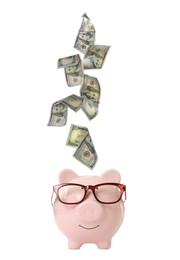 Dollar banknotes falling into pink piggy bank with glasses on white background