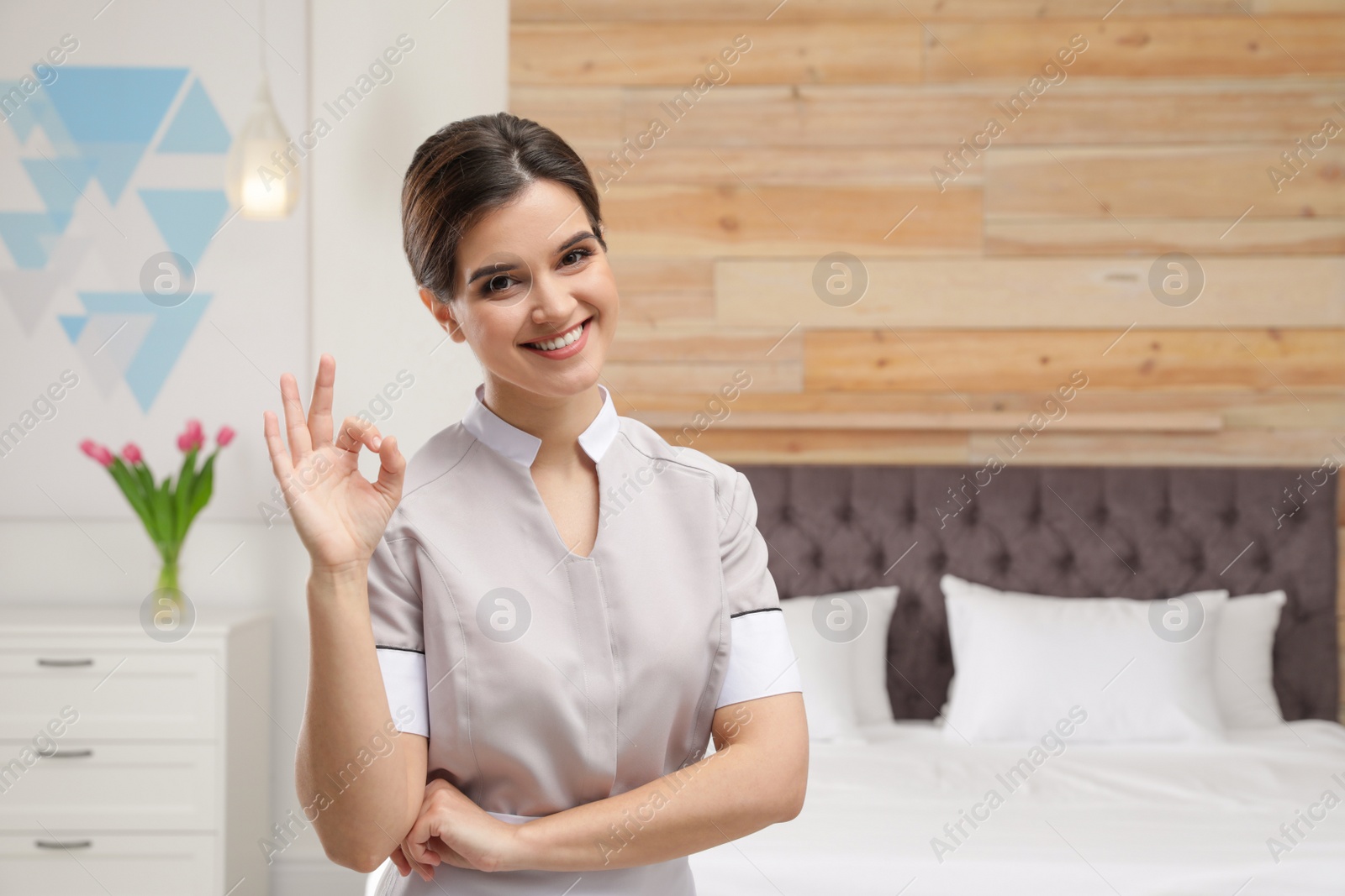 Photo of Young maid showing OK gesture in hotel room. Space for text