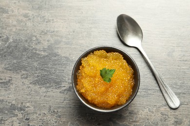 Photo of Fresh pike caviar in bowl and spoon on grey table, top view. Space for text