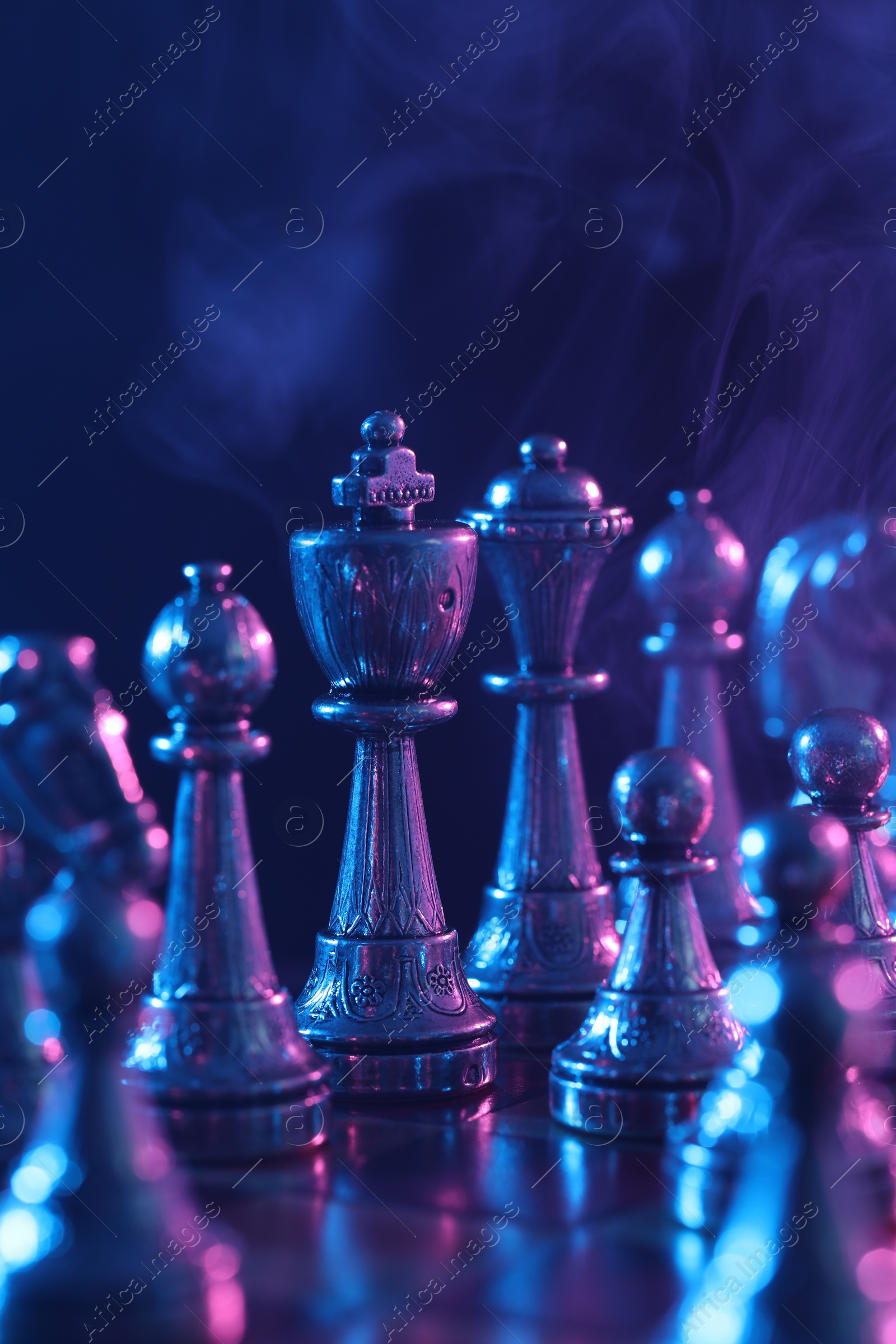 Photo of Chess pieces on checkerboard in color light, selective focus