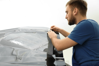 Worker tinting car window with foil in workshop