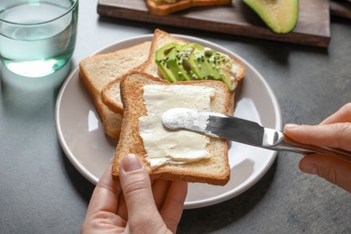 Photo of Woman spreading butter on toasted bread at table, closeup