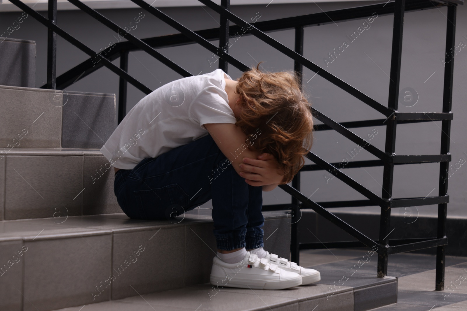 Photo of Child abuse. Upset boy sitting on stairs