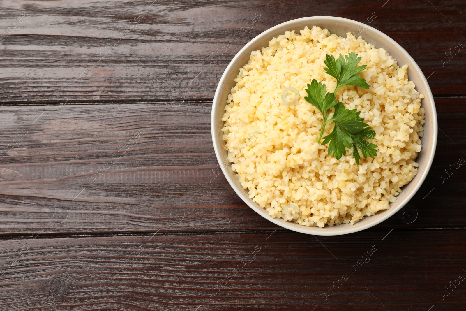 Photo of Delicious bulgur with parsley in bowl on wooden table, top view. Space for text