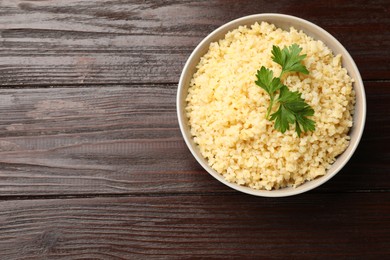 Photo of Delicious bulgur with parsley in bowl on wooden table, top view. Space for text