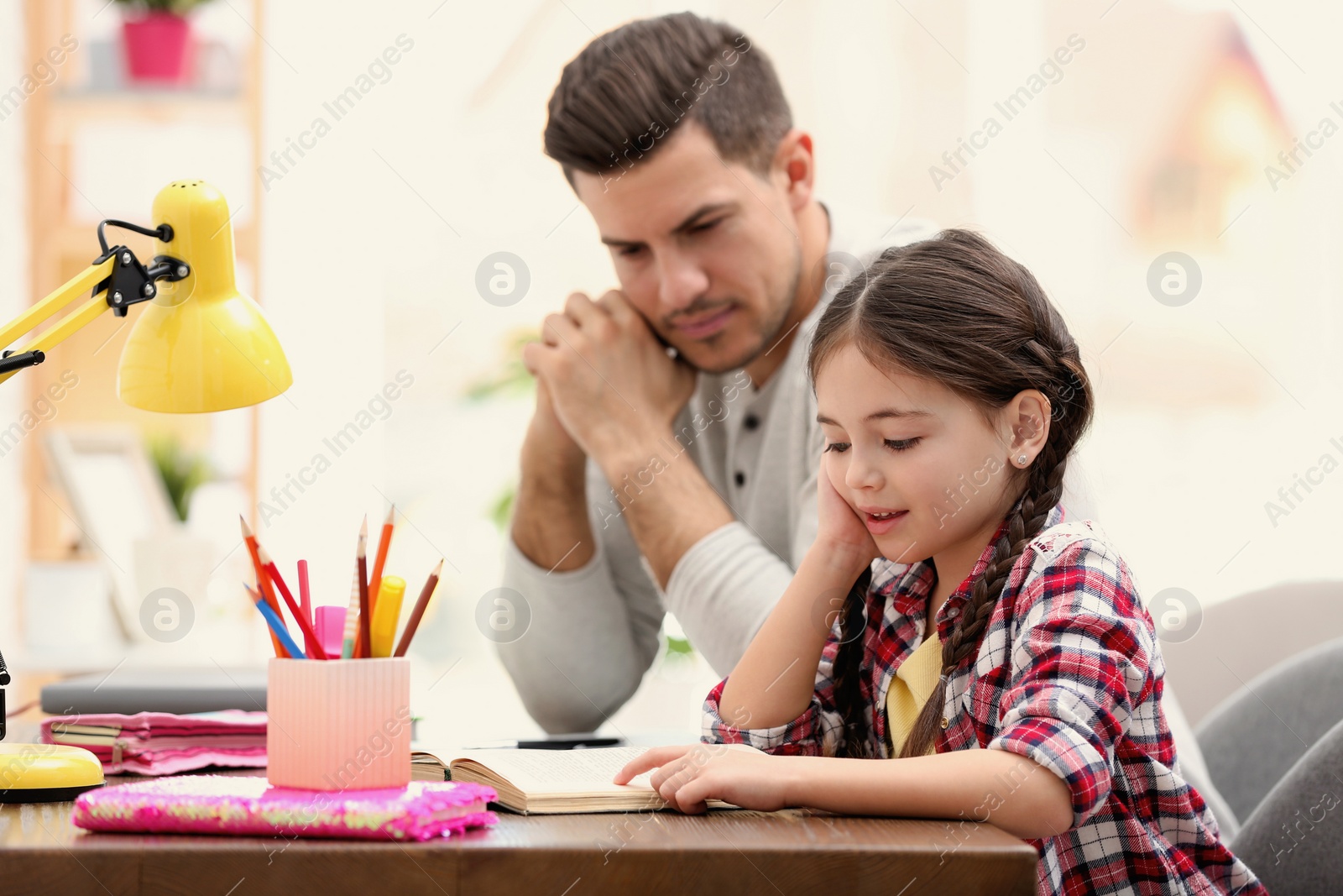 Photo of Man helping his daughter with homework at table indoors