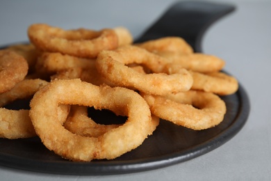 Slate plate with fried onion rings on grey table, closeup