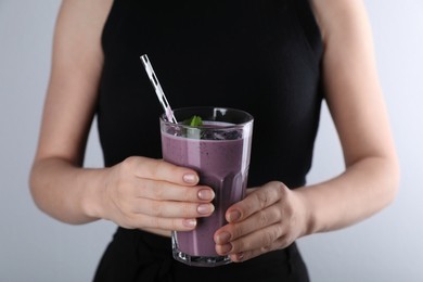 Photo of Woman with tasty blueberry smoothie against light grey background, closeup