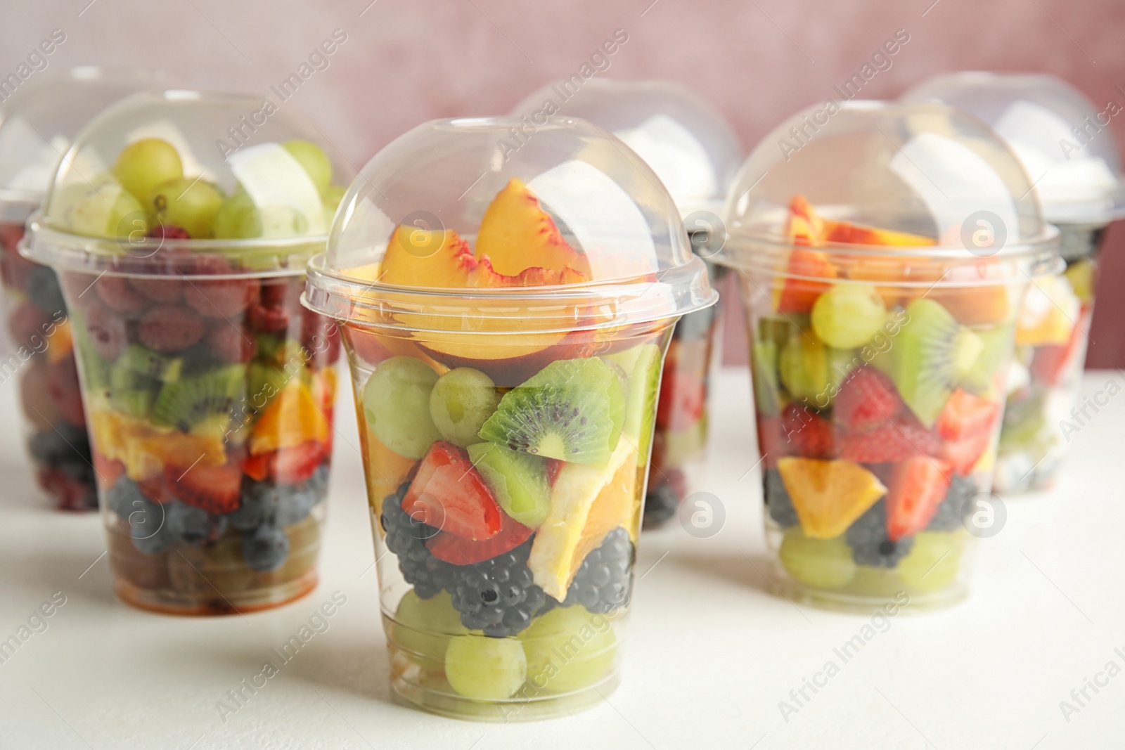 Photo of Fresh tasty fruit salad in plastic cups on white table