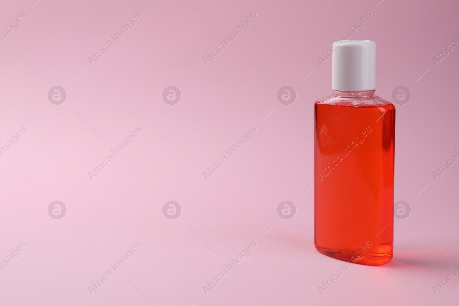 Photo of Fresh mouthwash in bottle on pink background. Space for text