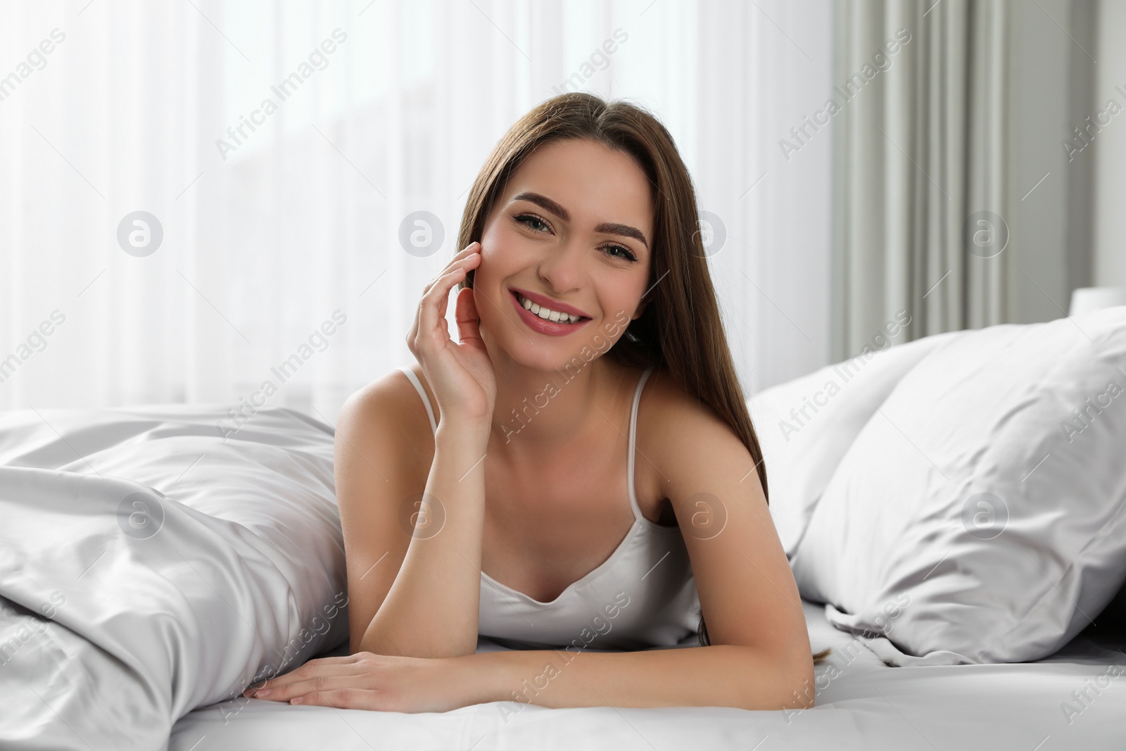 Photo of Young woman lying on comfortable bed with silky linens