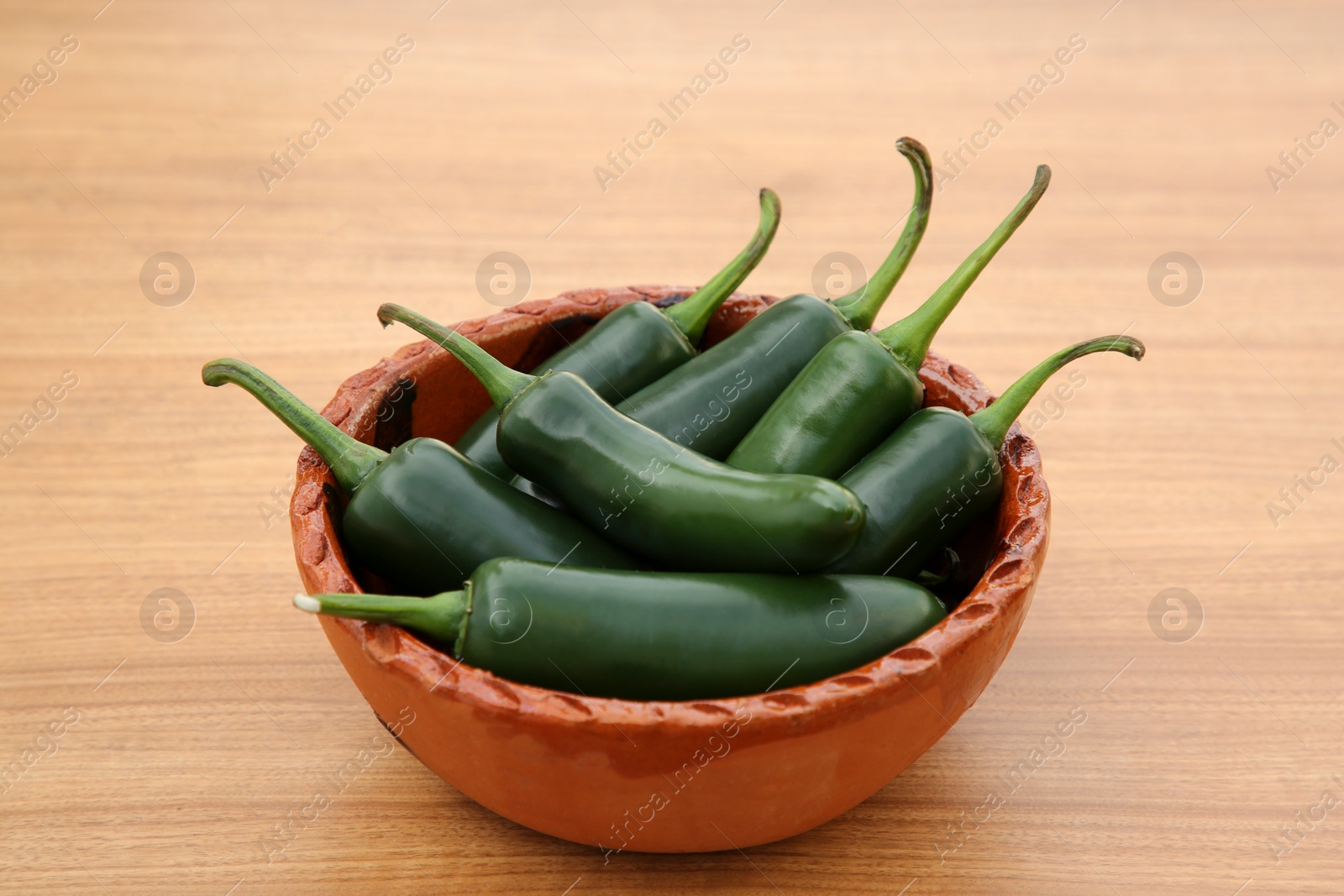 Photo of Bowl of fresh green jalapeno peppers on wooden table