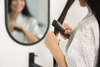Photo of Woman using hair iron near mirror indoors, closeup. Space for text