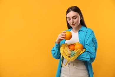 Photo of Woman with string bag of fresh oranges on orange background, space for text