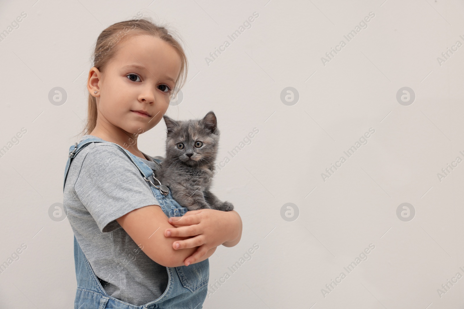 Photo of Cute little girl with kitten on light background, space for text. Childhood pet