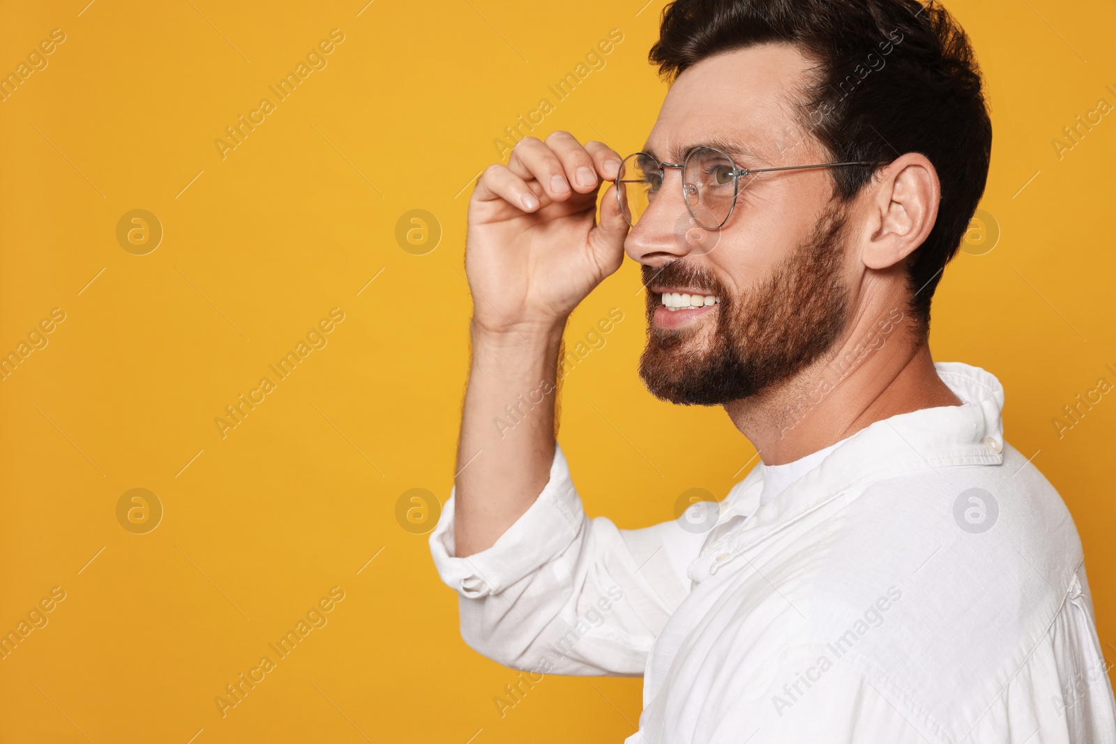 Photo of Profile portrait of smiling bearded man with glasses on orange background. Space for text