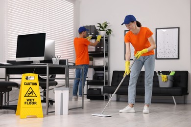 Photo of Cleaning service workers cleaning. Bucket with supplies and wet floor sign in office