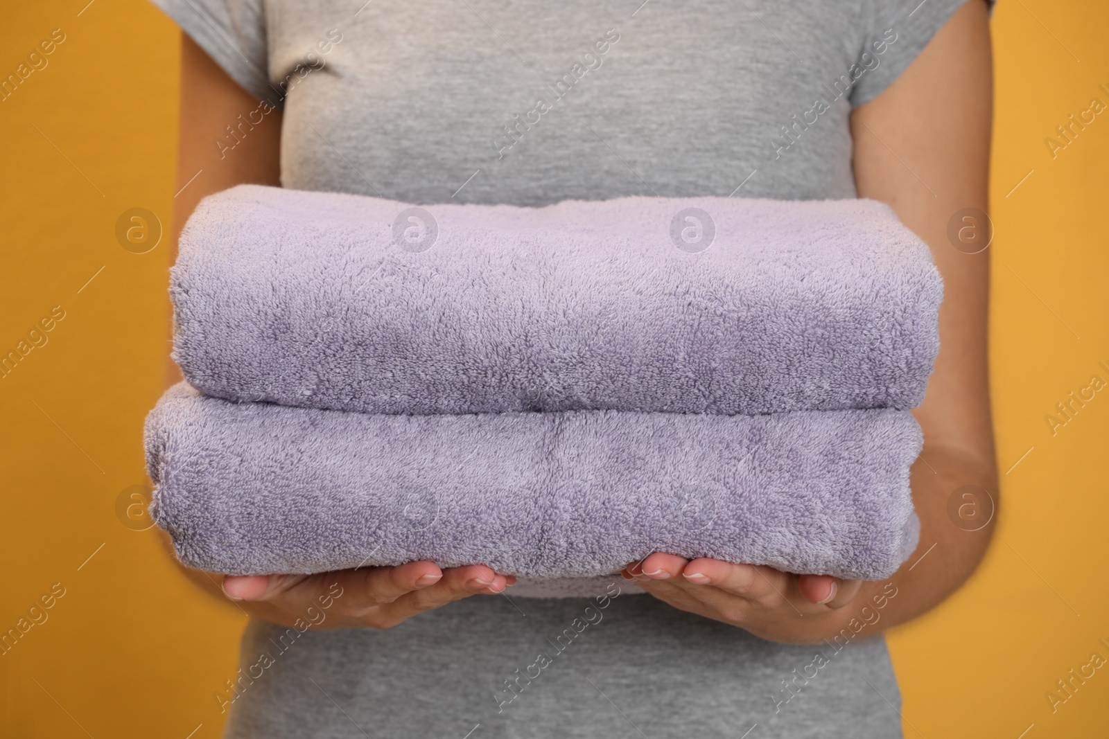 Photo of Woman holding fresh towels on orange background, closeup