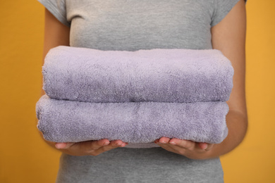 Photo of Woman holding fresh towels on orange background, closeup