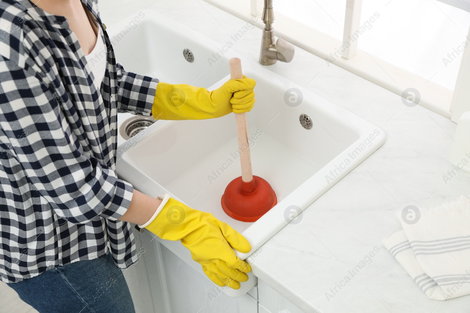 Photo of Woman using plunger to unclog sink drain in kitchen, closeup