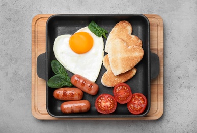 Romantic breakfast with fried sausages, heart shaped egg and toasts on grey table, top view. Valentine's day celebration