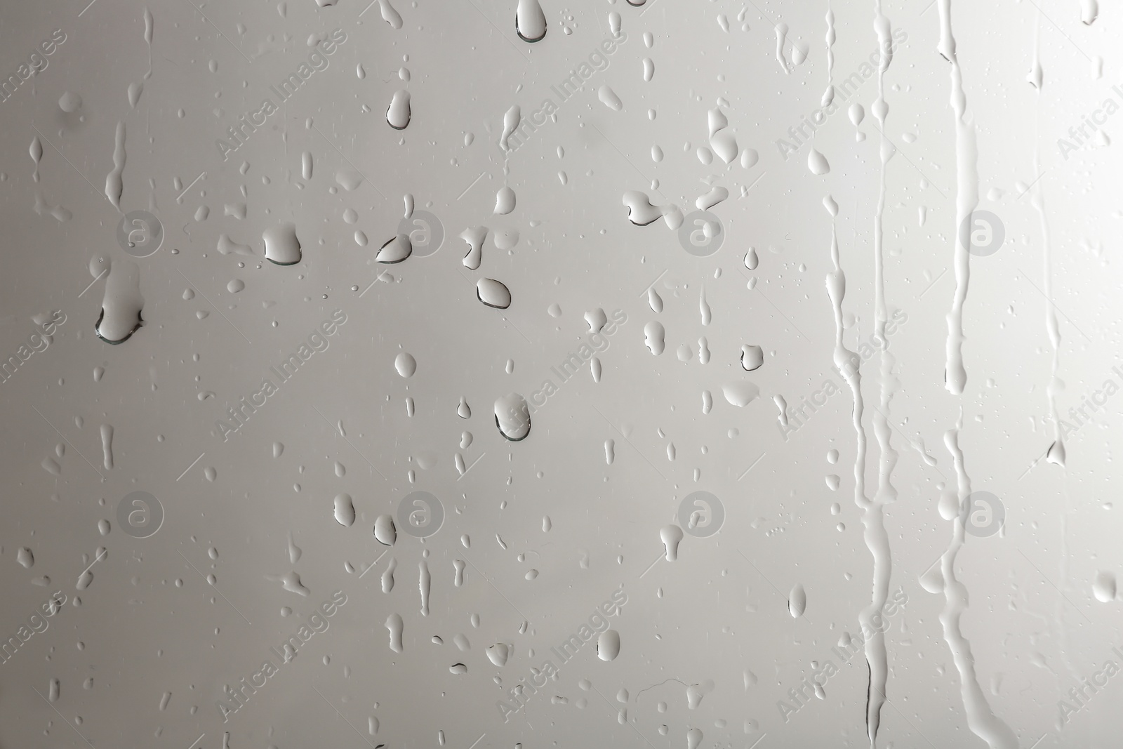 Photo of Glass with rain drops against light background