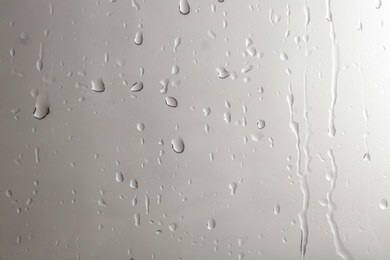 Photo of Glass with rain drops against light background