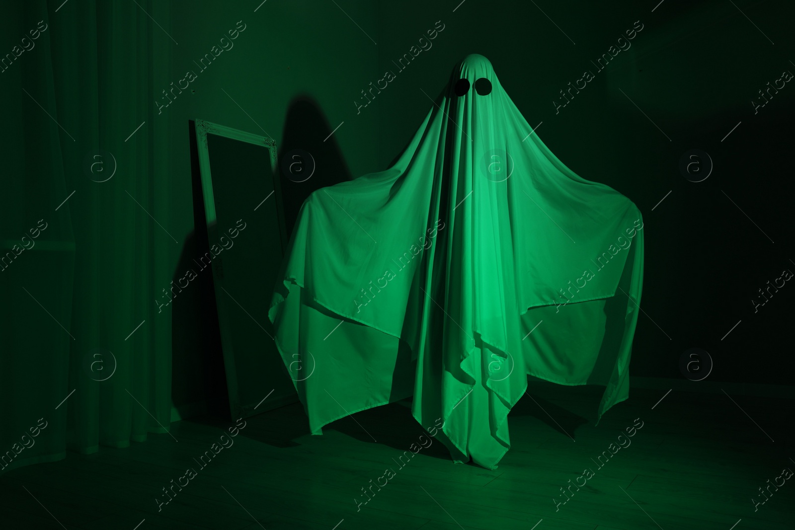 Photo of Creepy ghost. Woman covered with sheet in green light