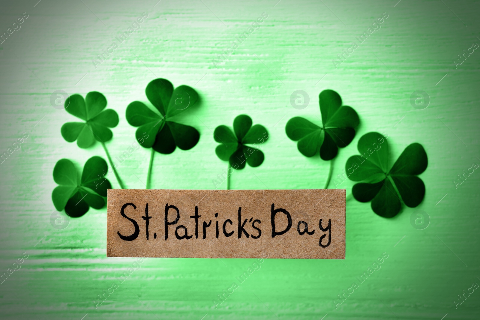 Image of Clover leaves and card with text ST. PATRICK'S DAY on green wooden table, flat lay