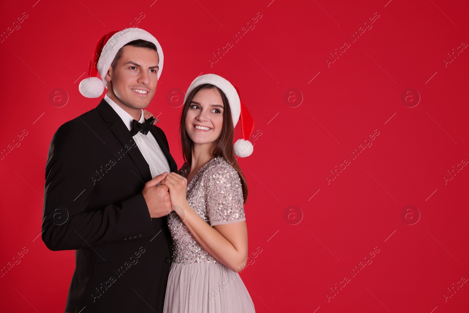 Photo of Beautiful happy couple in Christmas hats on red background. Space for text