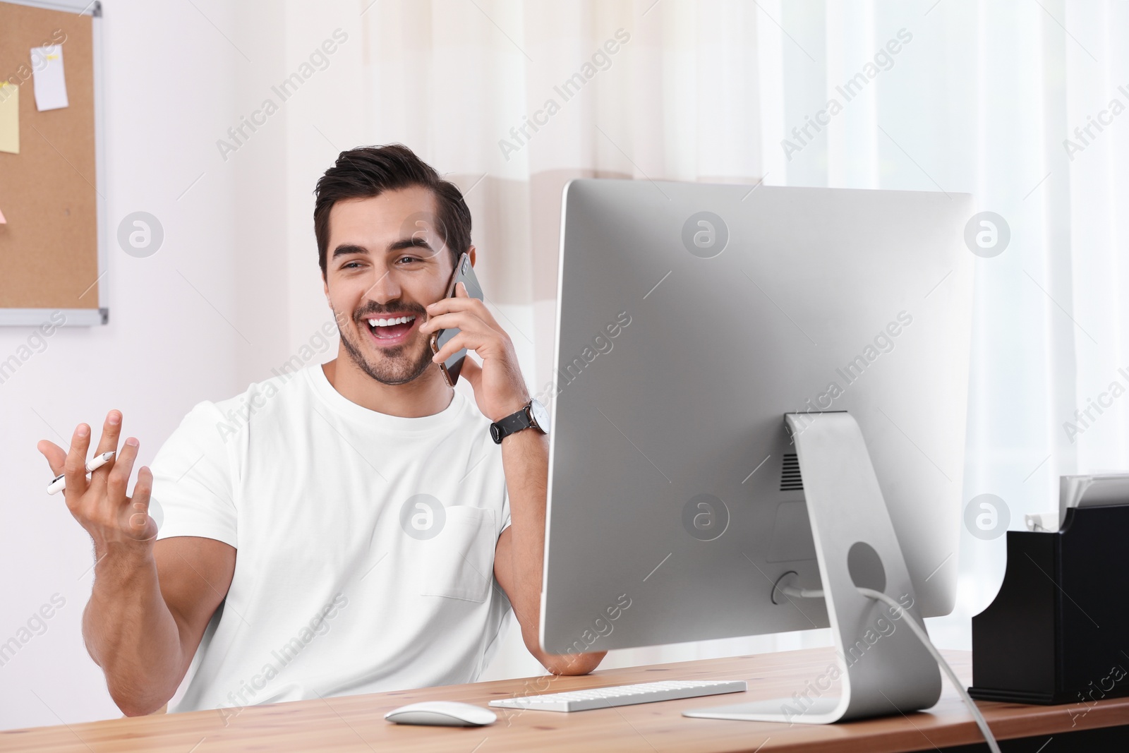 Photo of Handsome young man working with smartphone and computer at table in office