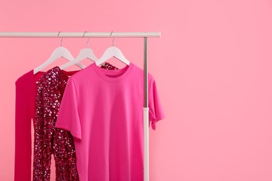 Photo of Rack with different stylish women`s clothes on pink background, space for text