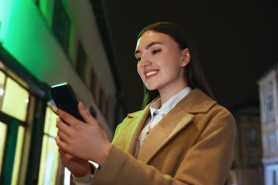 Photo of Smiling woman using smartphone on night city street
