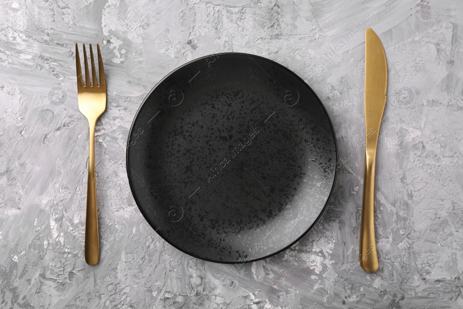 Photo of Elegant setting with golden cutlery on grey textured table, flat lay