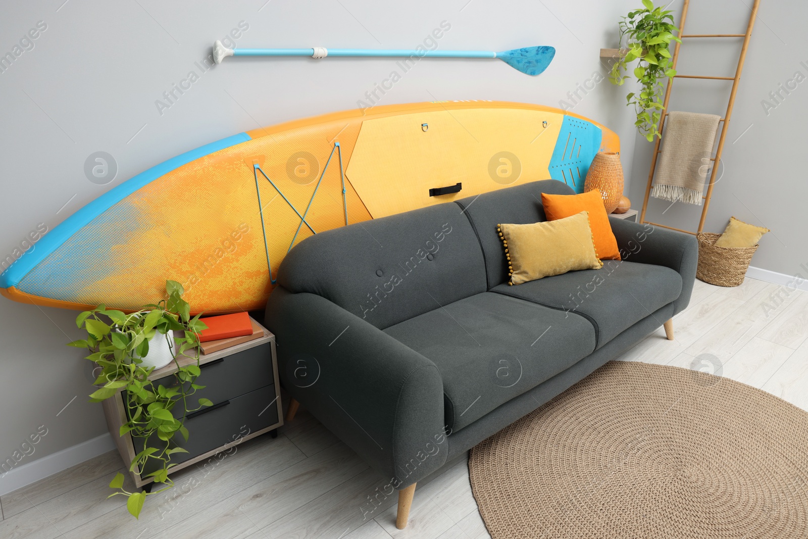 Photo of SUP board, paddle and stylish sofa in living room. Interior design