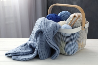 Photo of Soft woolen yarns with knitting needles and sweater on white table indoors