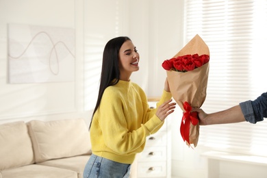 Happy woman receiving red tulip bouquet from man at home. 8th of March celebration