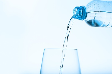 Pouring water from bottle into glass against blue background. Refreshing drink