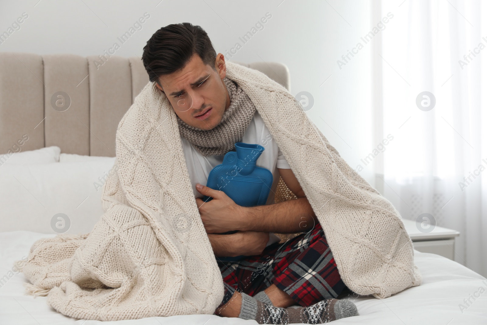 Photo of Ill man with hot water bottle suffering from cold at home