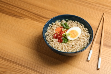 Bowl of noodles with broth, egg, vegetables and chopsticks served on wooden table. Space for text